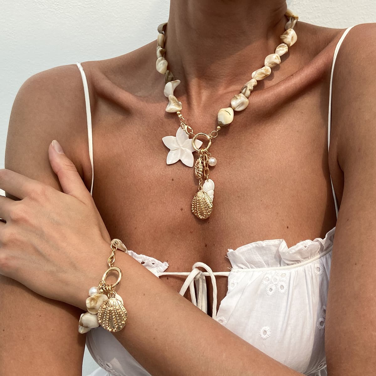 Handcrafted natural irregular shell bead collarbone necklace matching bracelet jewelry set for summer beach vacation, decorated with white shell flower, starfish, conch and textured scallop alloy pendants. Classic natural ocean element design with fresh sweet boho vacation style, adjustable length fits all neck & wrist sizes, ideal matching accessory for swimsuits, camisoles and casual travel outfits, perfect coastal holiday statement jewelry for women.
